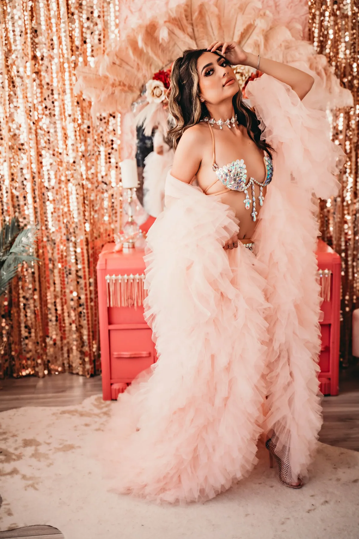 A Velvet Cowgirl client in a pink feather robe, posed confidently against shimmering rose-gold curtains